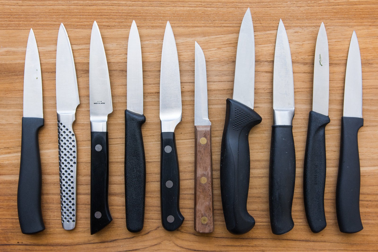 A sharp paring knife sits on a wooden board next to fresh ingredients.