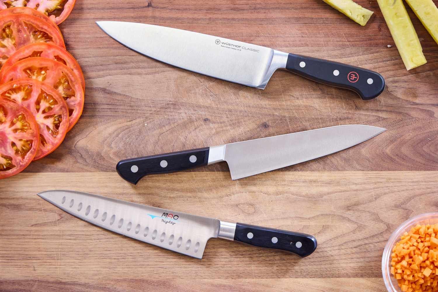 A sharp professional chef knife sits on a wooden board with fresh kitchen ingredients.
