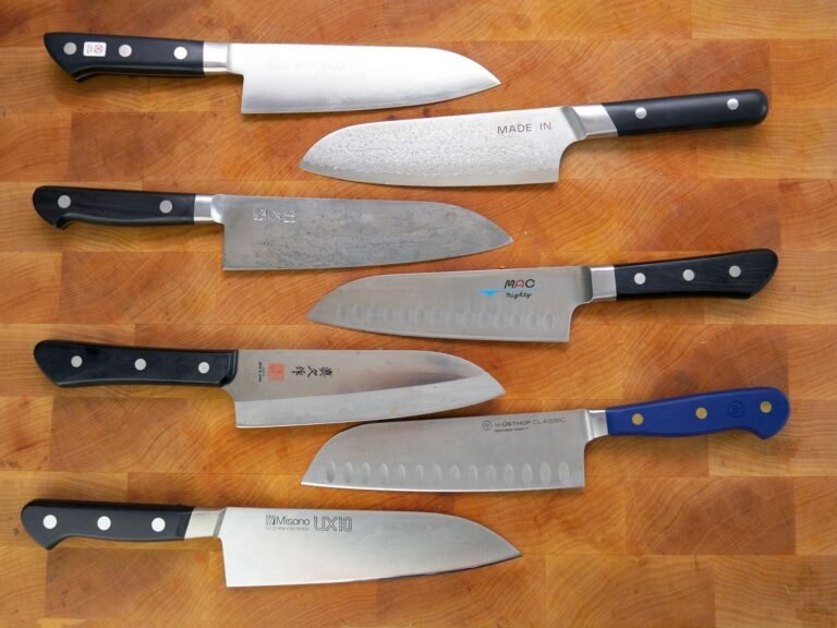 A sharp santoku knife sits on a wooden board with fresh kitchen ingredients.